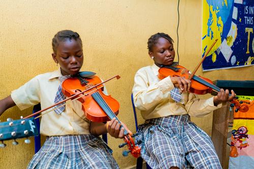 Two female college students playing the violin during a music lesson