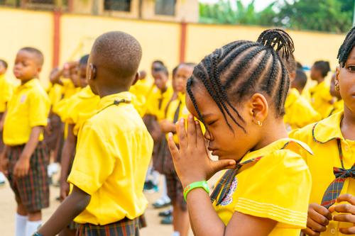 A female primary student clasping her hands during prayer at assembly