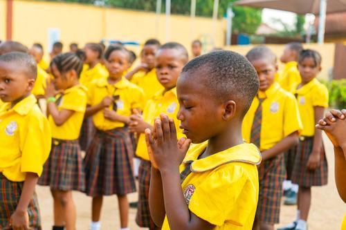 A female primary student clasping her hands during prayer at assembly