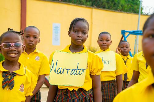 A female primary student with a narrator tag during a presentation on the assembly ground