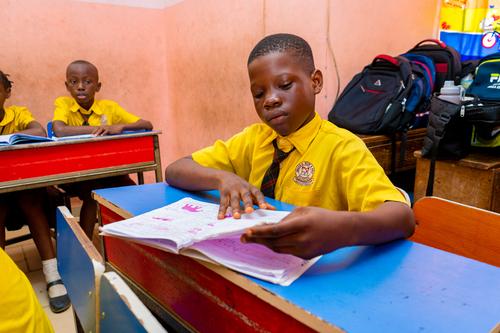 A male primary pupil reading a textbook in class